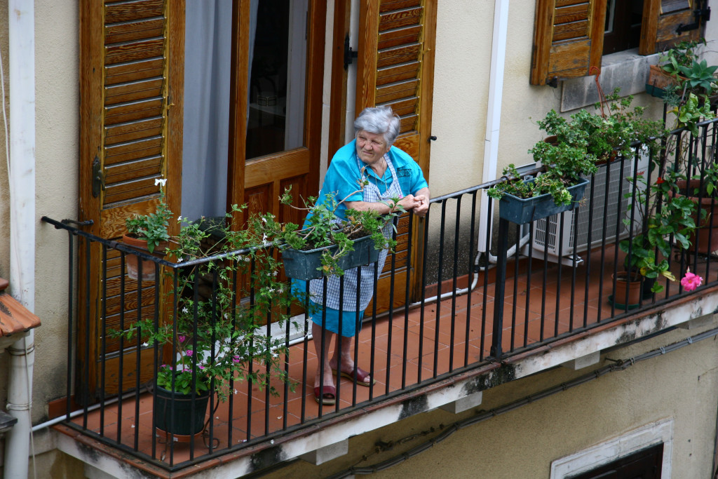Alte Sizilianerin in blauer Schürze schaut kritisch vom Balkon runter