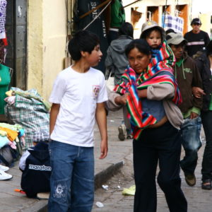 Auf den Straßen von Cuzco - Mutter trägt ihr Kind im peruanischen Tragetuch aus buntem Mantastoff